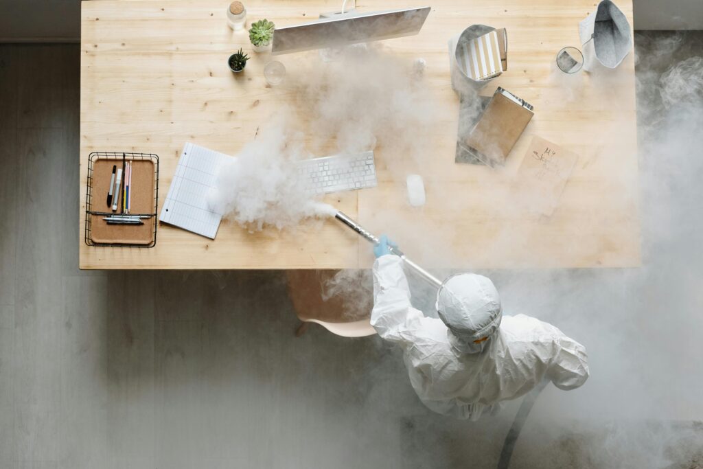 An individual disinfects a workspace using fumigation, wearing full protective gear for safety.